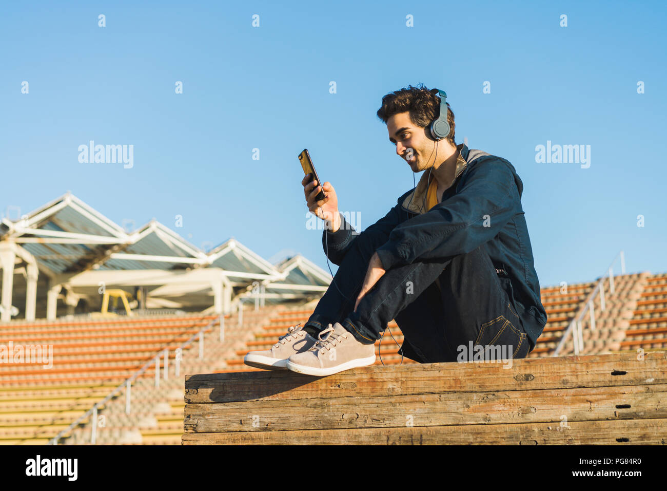 Man with headphones sitting on wood stack, using smartphone Stock Photo