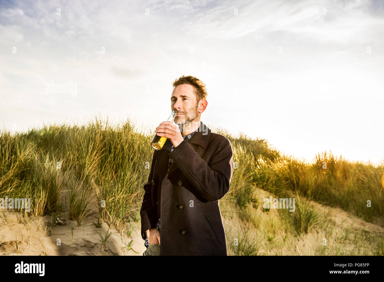 Smiling woman drinking a beer in dunes Stock Photo