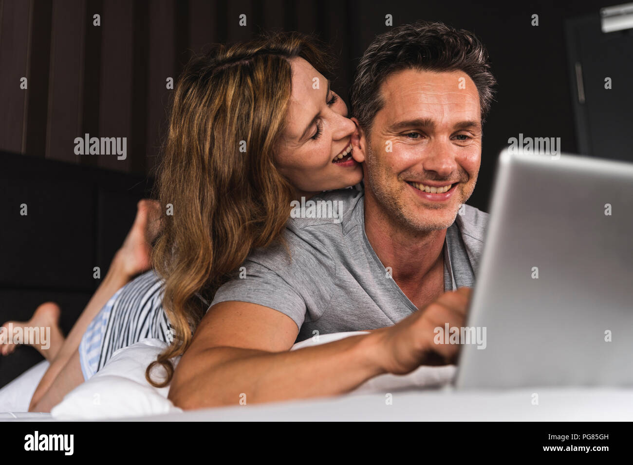 Happy couple lying on bed at home with laptop Stock Photo - Alamy