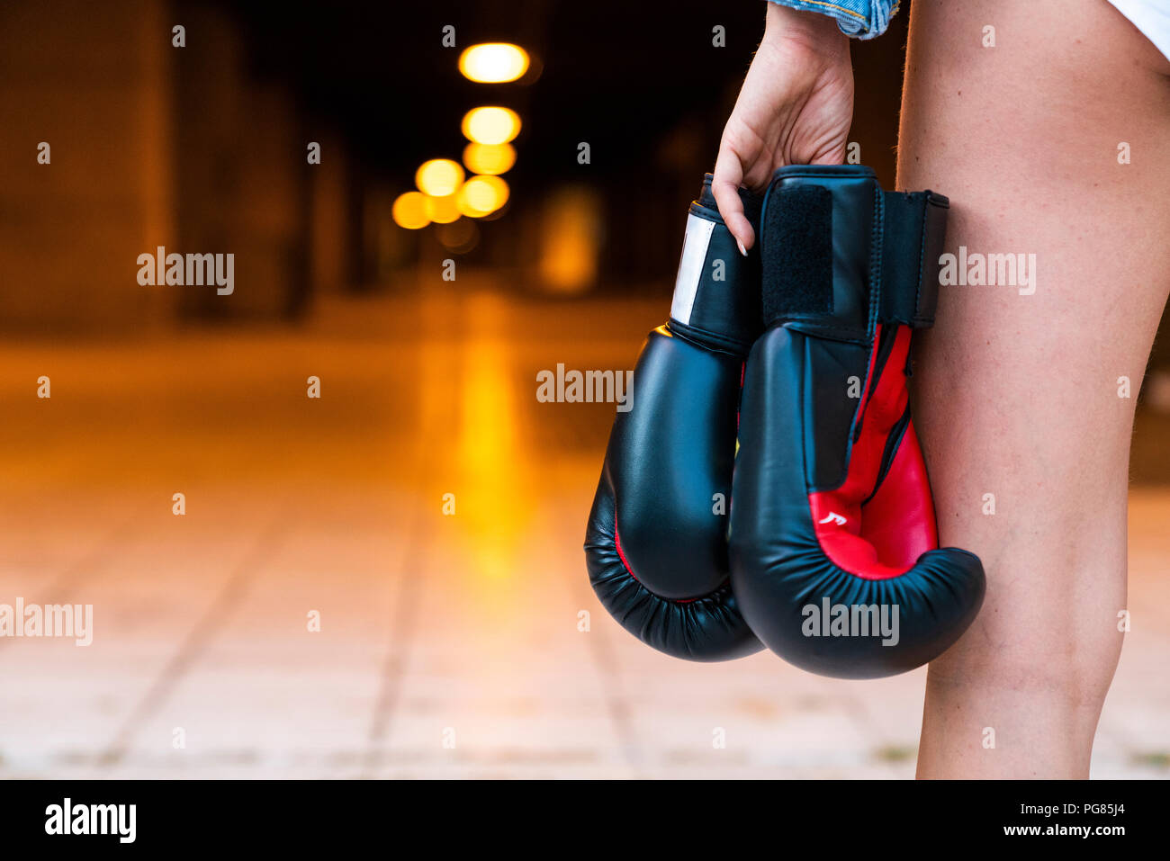 Close-up of woman holding boxing gloves at illuminated underpass Stock Photo