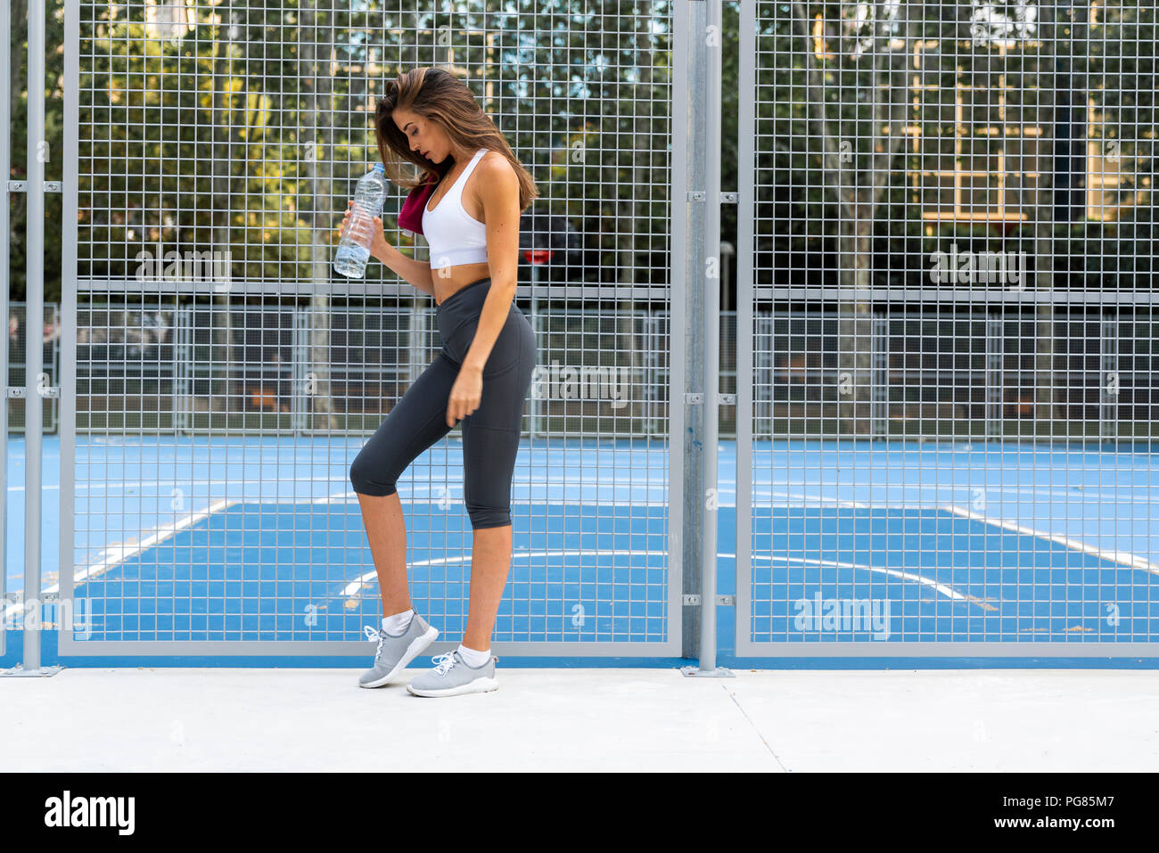 Sportive young woman standing at sports field holding water bottle ...
