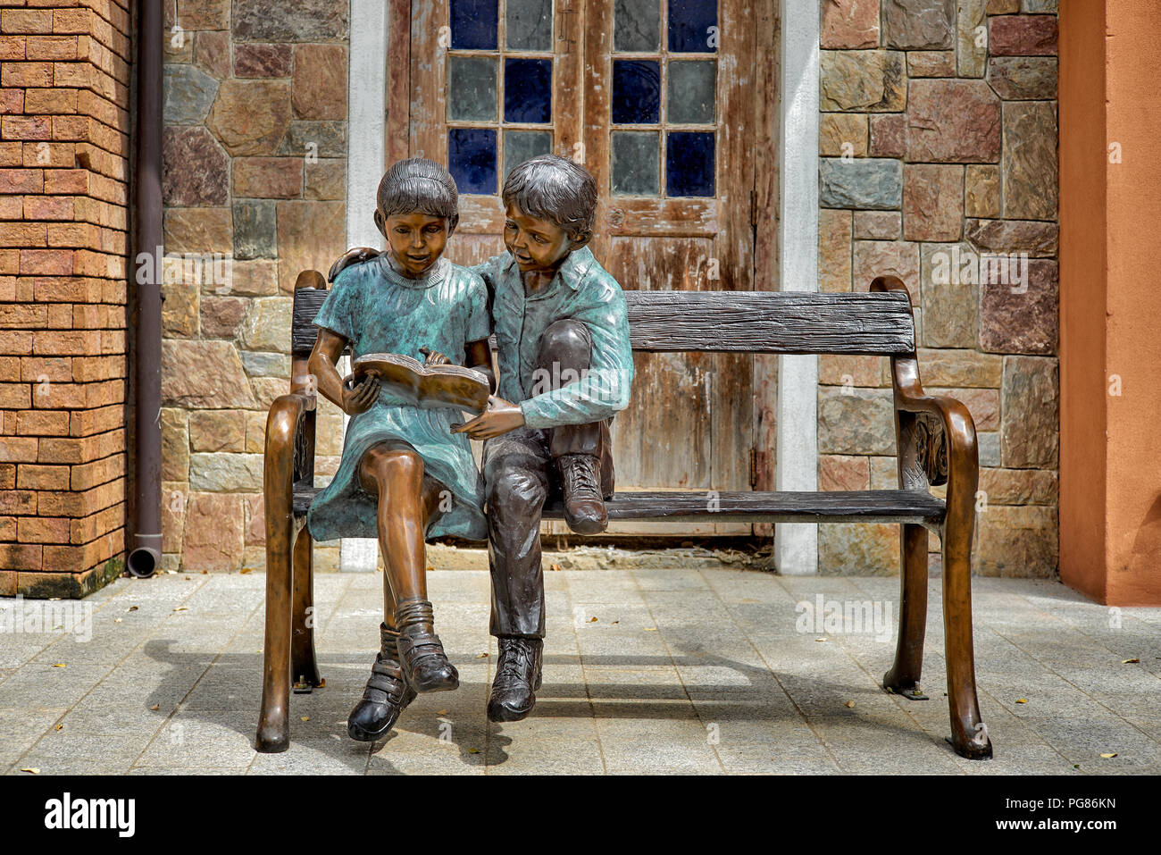Statue boy and girl sitting on a bench, reading book, together. togetherness Stock Photo