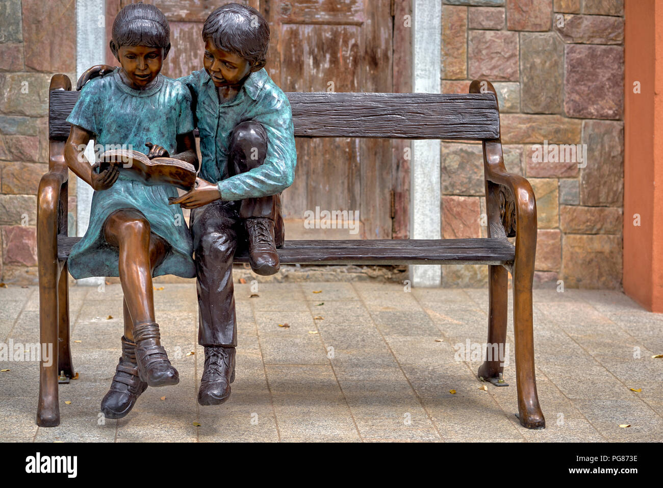 Statue boy and girl sitting on a bench, reading book, together. togetherness Stock Photo