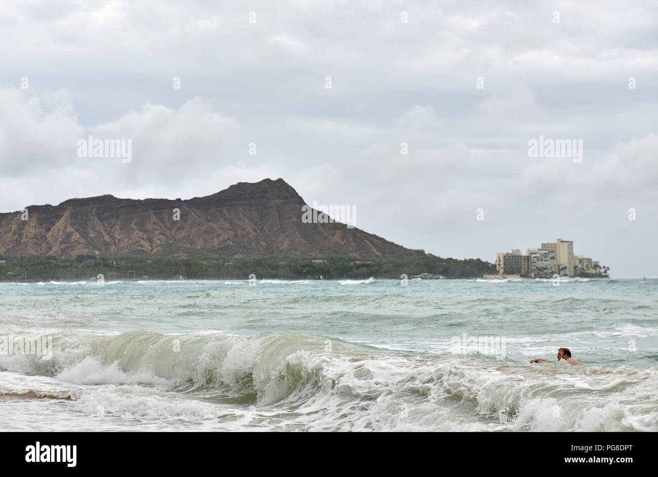 Honolulu, USA. 23rd Aug, 2018. A man surfs in the ocean at Waikiki beach in Honolulu of Hawaii, the United States, Aug. 23, 2018. Hurricane Lane, predicted as the biggest weather threat to Hawaii in decades, moved perilously close to the Aloha State Thursday morning, triggering heavy rain, landslide and flooding. Credit: Sun Ruibo/Xinhua/Alamy Live News Stock Photo