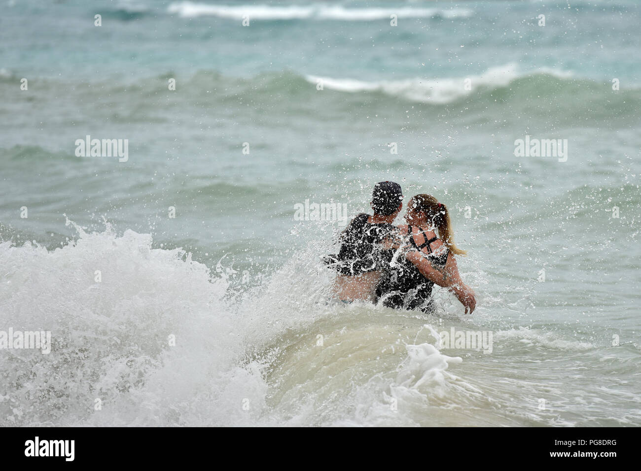 Honolulu, USA. 23rd Aug, 2018. A young couple get caught by a strong wave at Waikiki beach in Honolulu of Hawaii, the United States, Aug. 23, 2018. Hurricane Lane, predicted as the biggest weather threat to Hawaii in decades, moved perilously close to the Aloha State Thursday morning, triggering heavy rain, landslide and flooding. Credit: Sun Ruibo/Xinhua/Alamy Live News Stock Photo