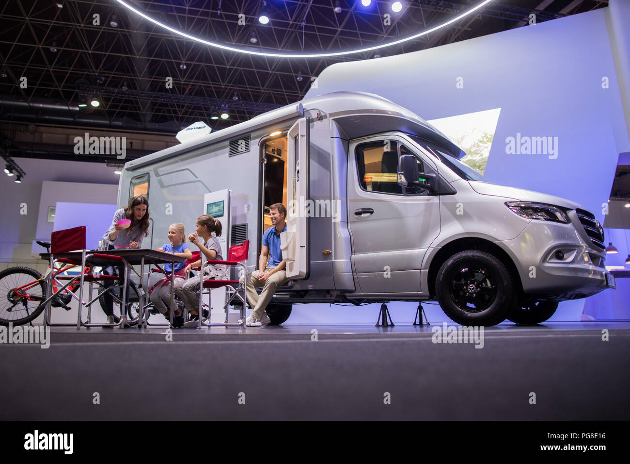 24 August 2018, Germany, Düsseldorf: Hilal (l) and Frank (r) and the  children Mathilde (l) and Lucie sit in front of the new Hymer Modern  Comfort. The world's largest camping fair Caravan