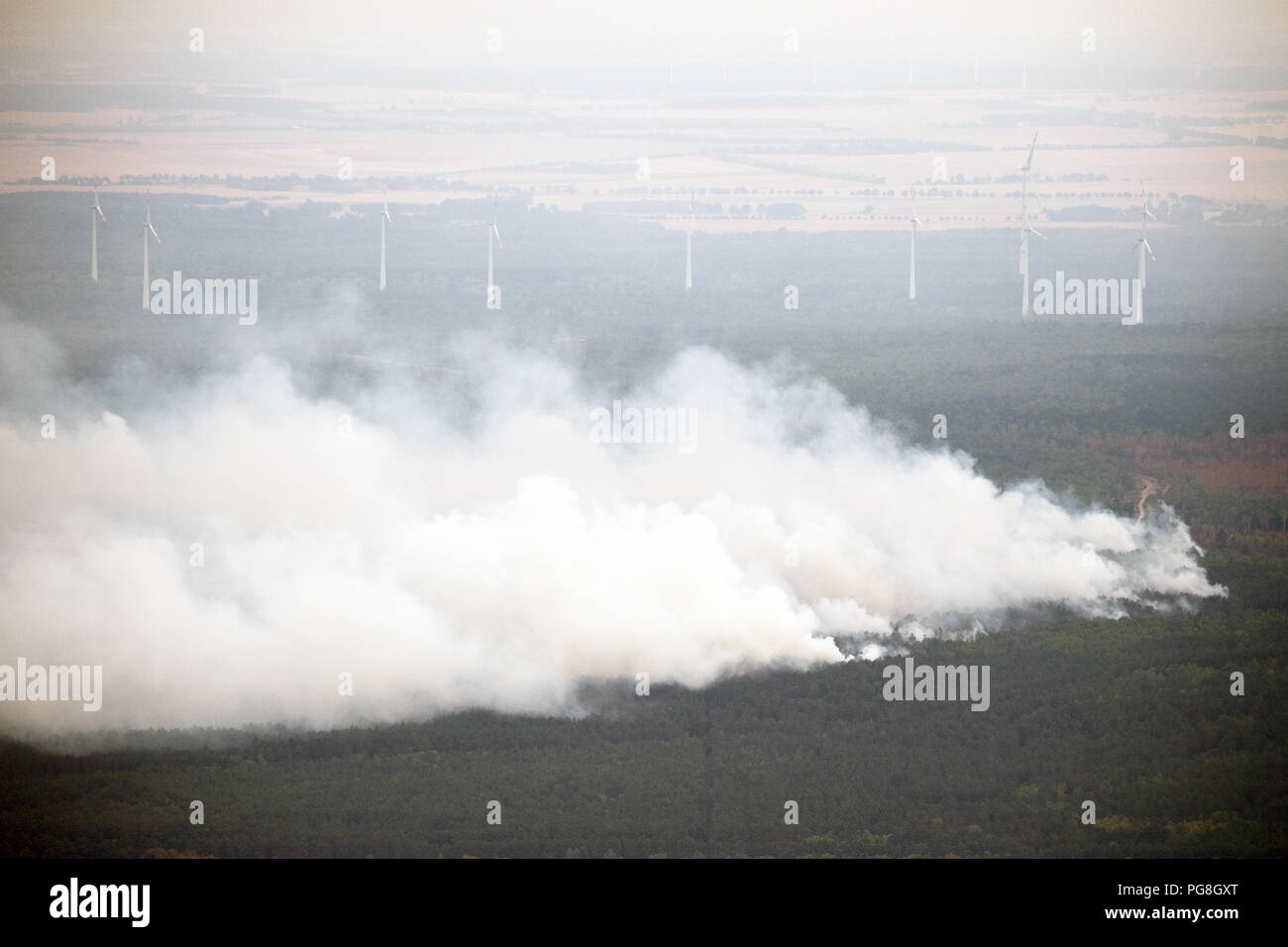 Frohnsdorf, Germany. 24th Aug, 2018. Wind turbines can be seen behind a burning forest. Hundreds of emergency forces contained the huge forest fire southwest of Berlin on Friday, but have not yet brought it under control. Credit: Ralf Hirschberger/dpa/Alamy Live News Stock Photo