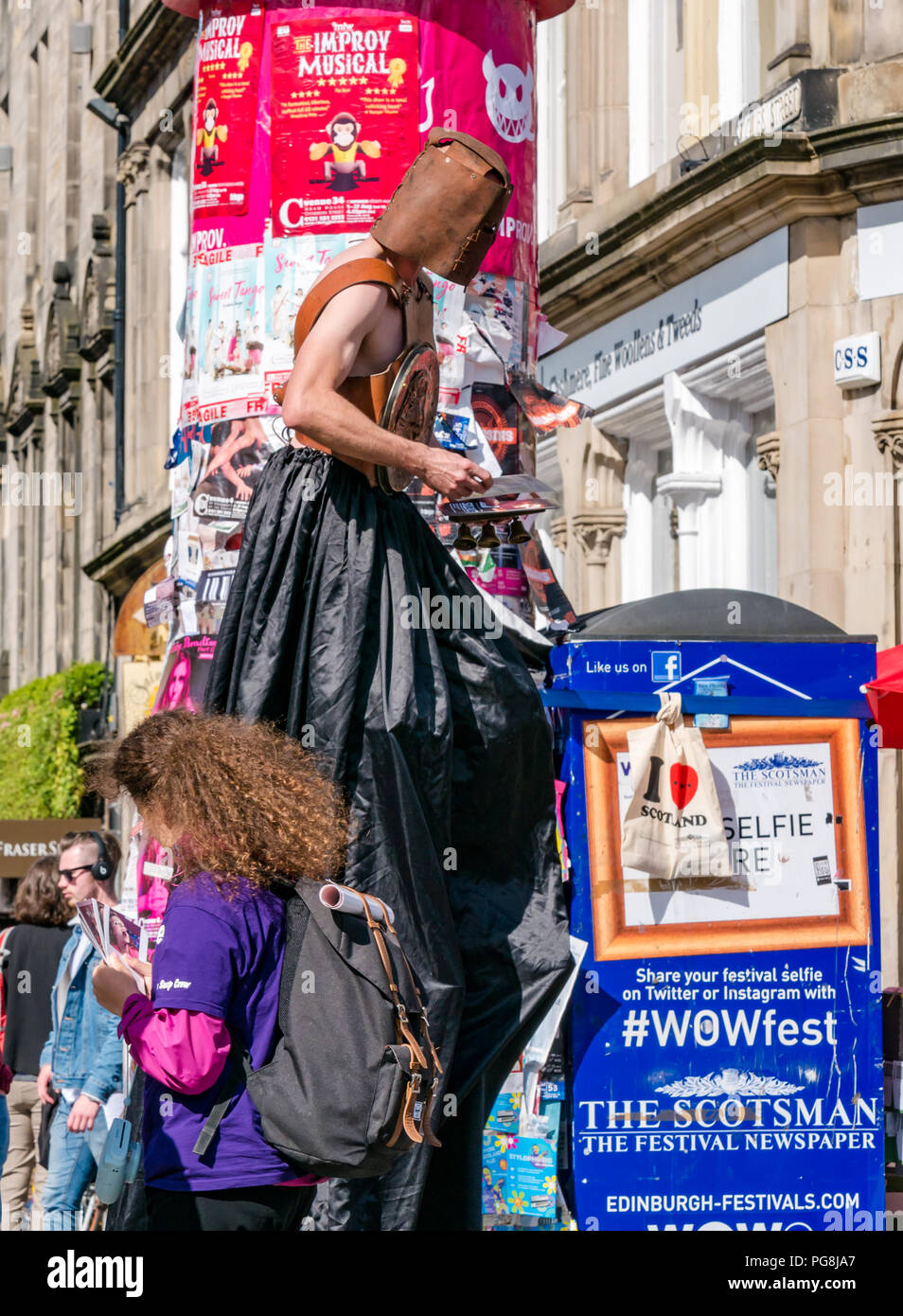 Edinburgh Fringe, Edinburgh, Scotland, UK. 24th August 2018.  The sun shone on Fringe goers and festival performers at the Virgin Money sponsored street venue on the Royal Mile as it nears its end. A man in costume walks on stilts among the festival crowd handing out fyers for the Fringe show Silence, a story of refugees caught in violence with dreams of escape Stock Photo