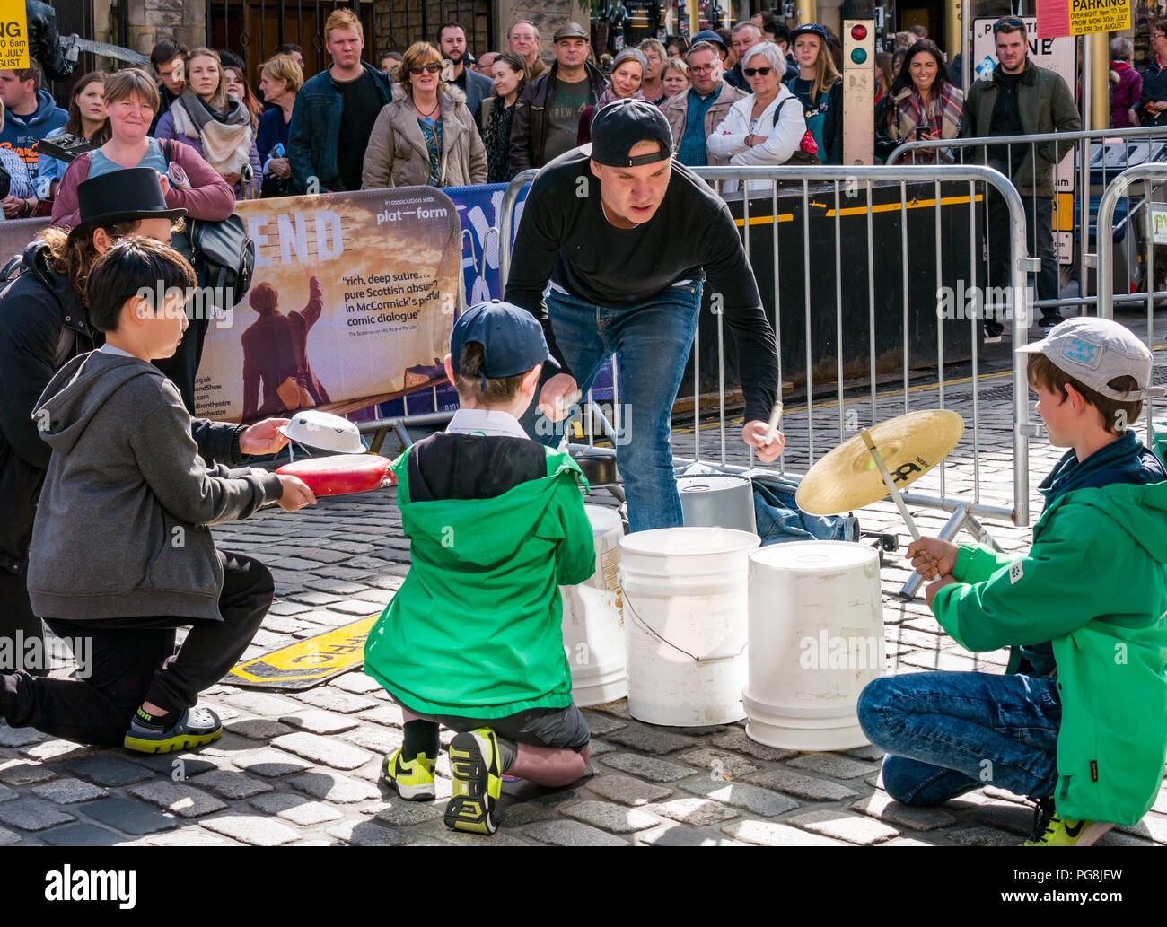 Edinburgh Fringe Festival, Edinburgh, Scotland, UK. 24th August 2018.  The sun shines on Fringe goers and a street performer at the Virgin Money sponsored street venue on the Royal Mile. A street busker called The Bucket Boy, aka Matthew Pretty, drums on buckets and pans and other objects and involves children in the crowd to hold objects for him to drum Stock Photo