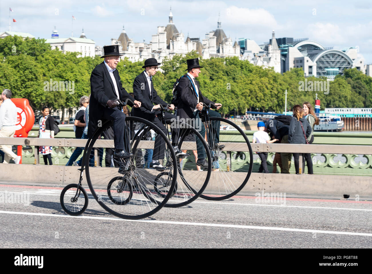 Three penny farthing cyclists ride across Westminster Bridge, London, UK. Gentlemen riders dressed in period costume. Penny farthings by UDC penny farthings, Unicycle Dot Com Stock Photo