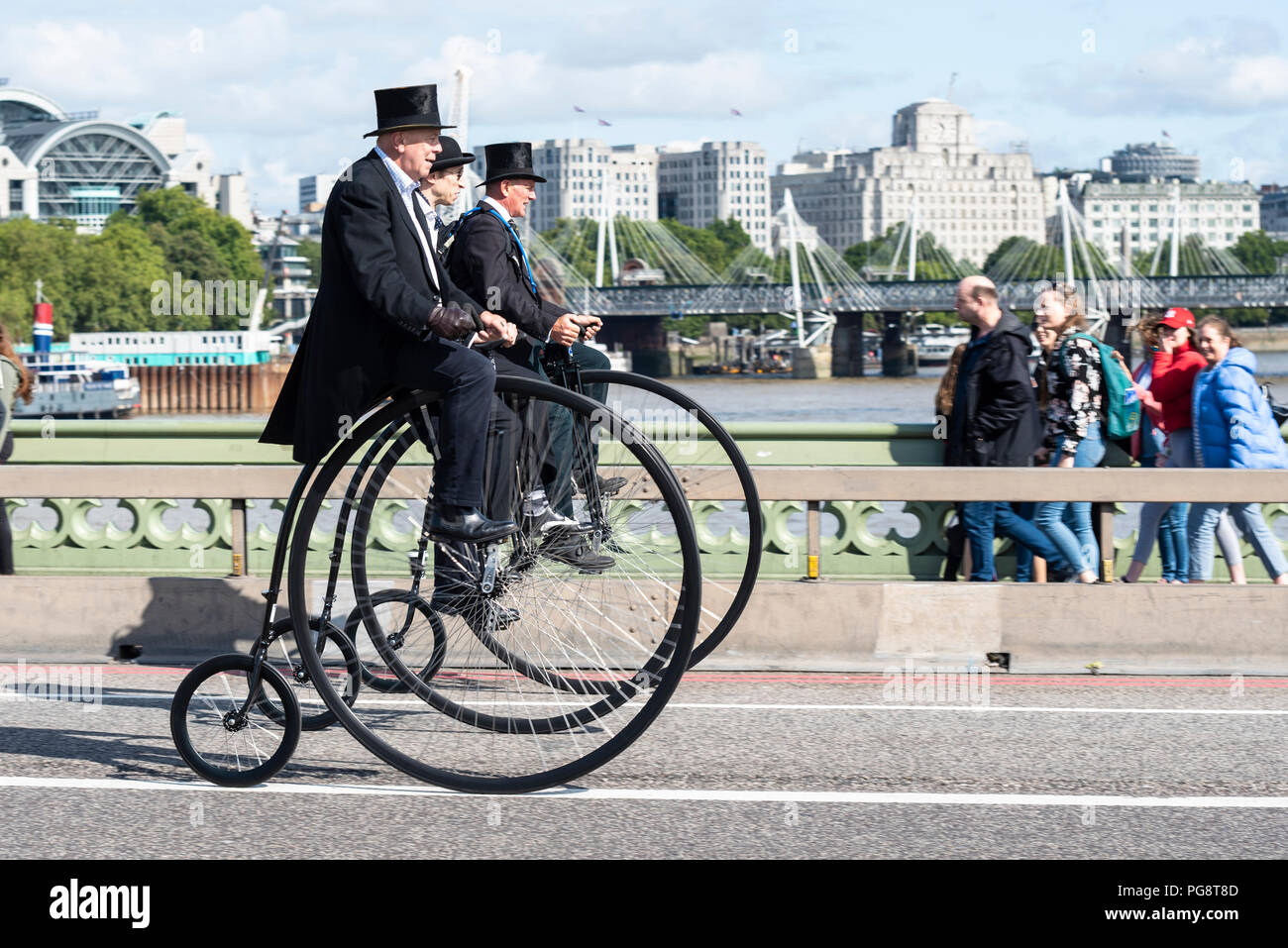 Three penny farthing cyclists ride across Westminster Bridge, London, UK. Gentlemen riders dressed in period costume. Penny farthings by UDC penny farthings, Unicycle Dot Com Stock Photo