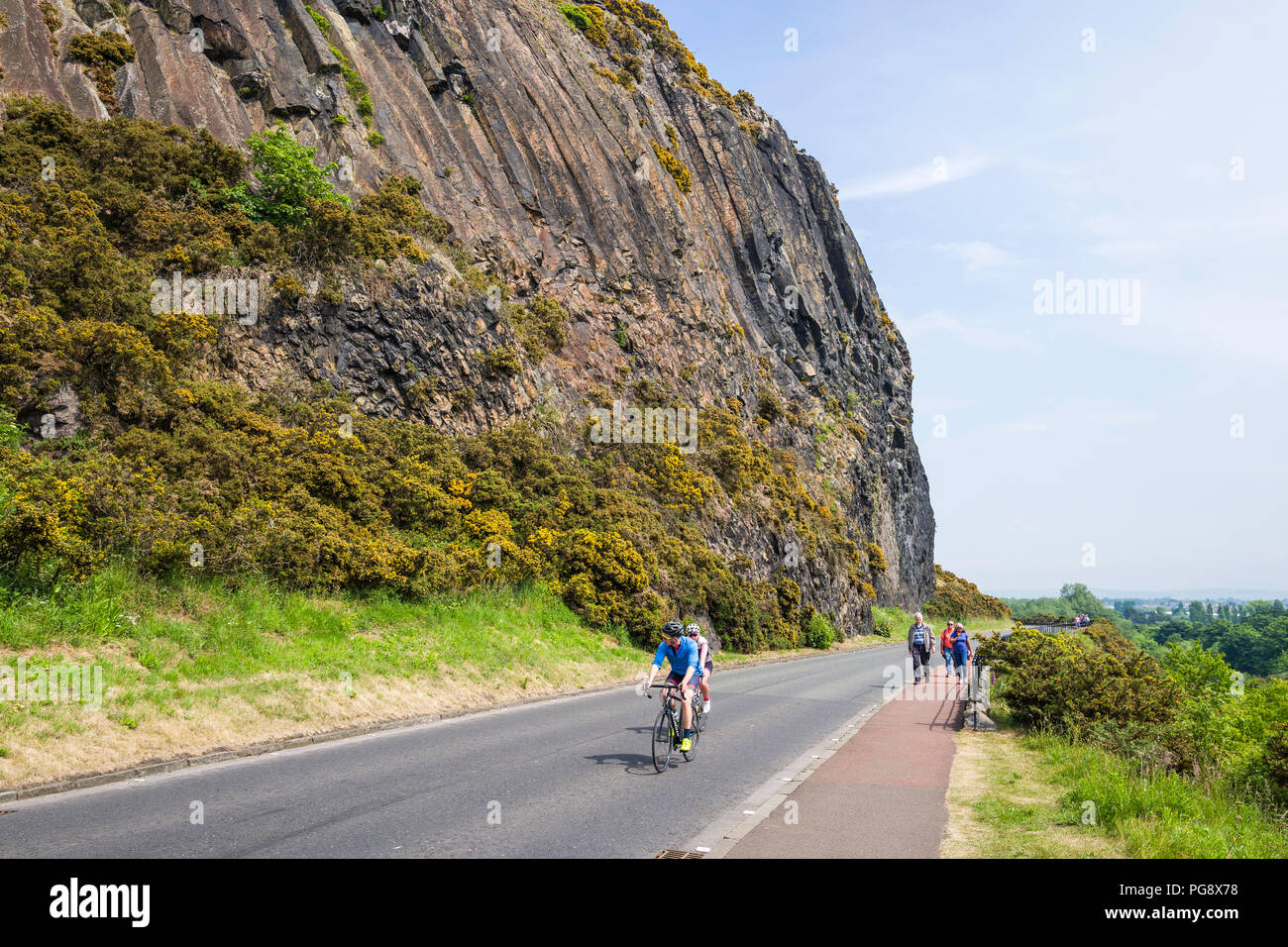 Cyclists and walkers on Duddingston Low Road beneath the cliffs of Arthur's Seat.  The road links Duddingston Village with central Edinburgh. Stock Photo