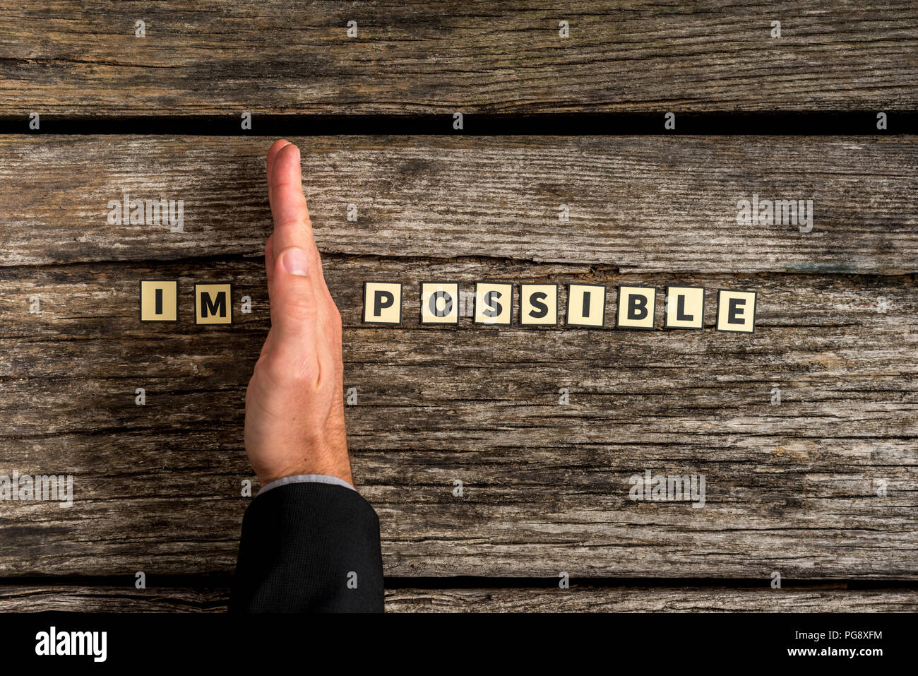 Hand dividing impossible letter tile sign into possible on textured wooden background Stock Photo