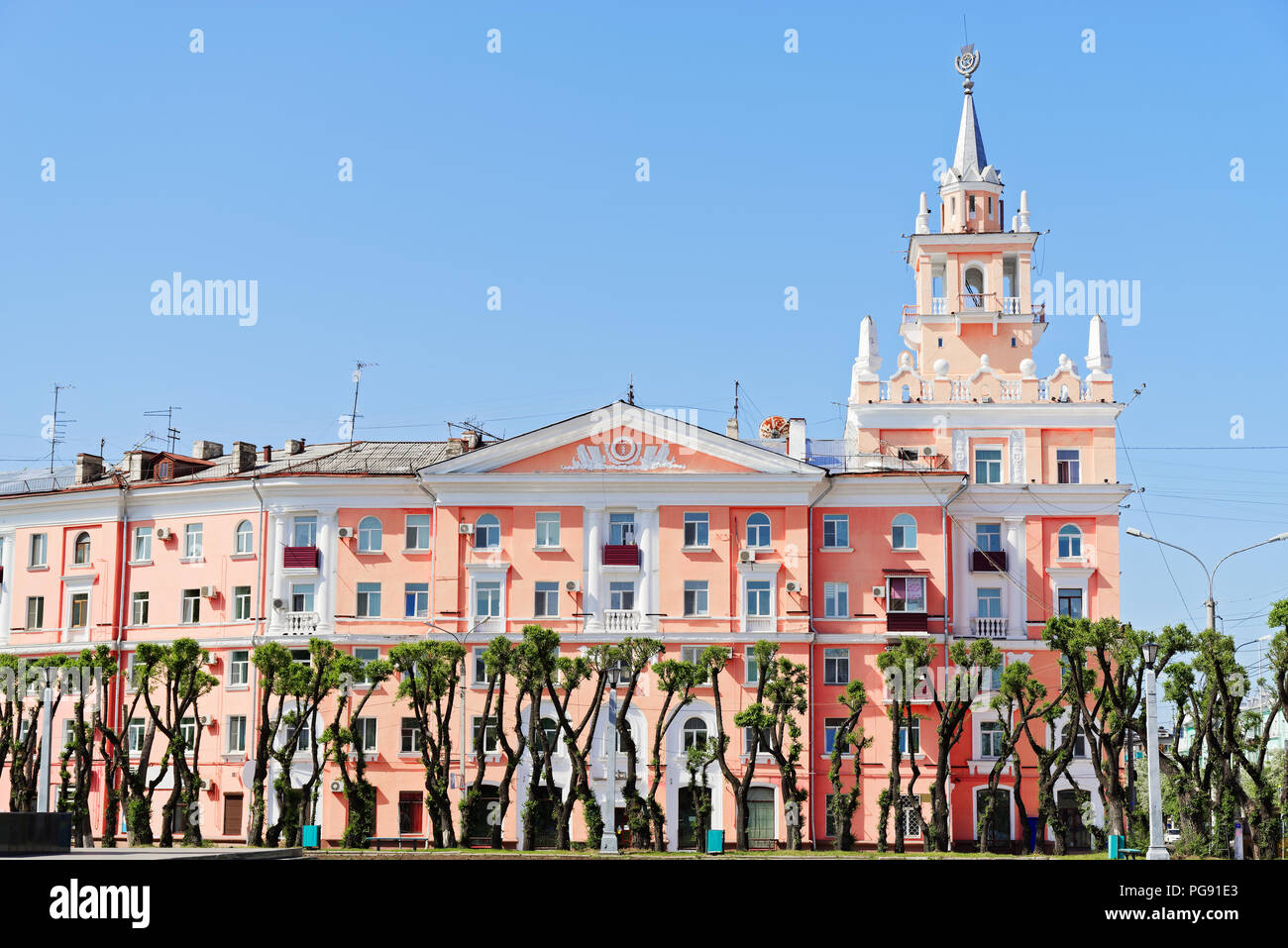 Beautiful pink building with spire against clear blue sky. This building is unofficial symbol of Komsomolsk-on-Amur Stock Photo