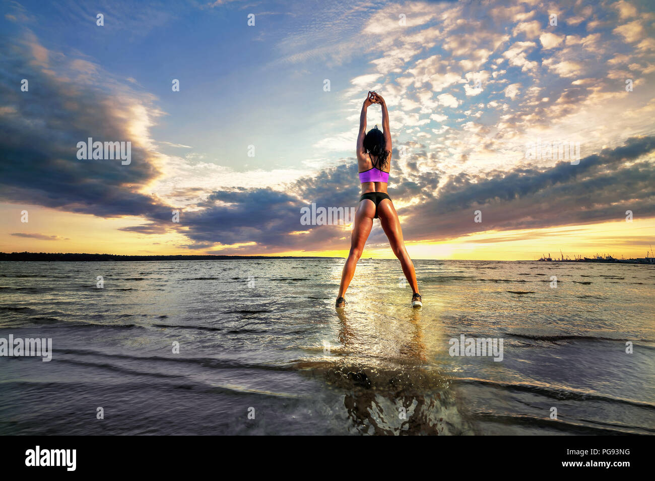 Young fitness woman doing exercise in shallow water on the beach at sunset Stock Photo