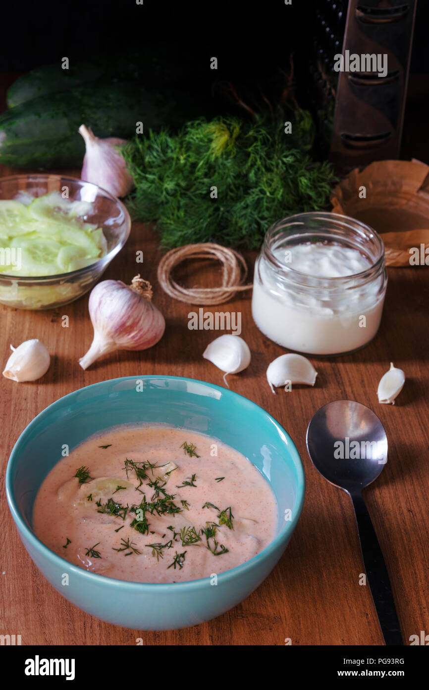 Food ingredients to make cucumber salad with yoghurt or sour cream dressing. Vegetable food ingredients, cucumber, garlic, dill, yoghurt on the table  Stock Photo