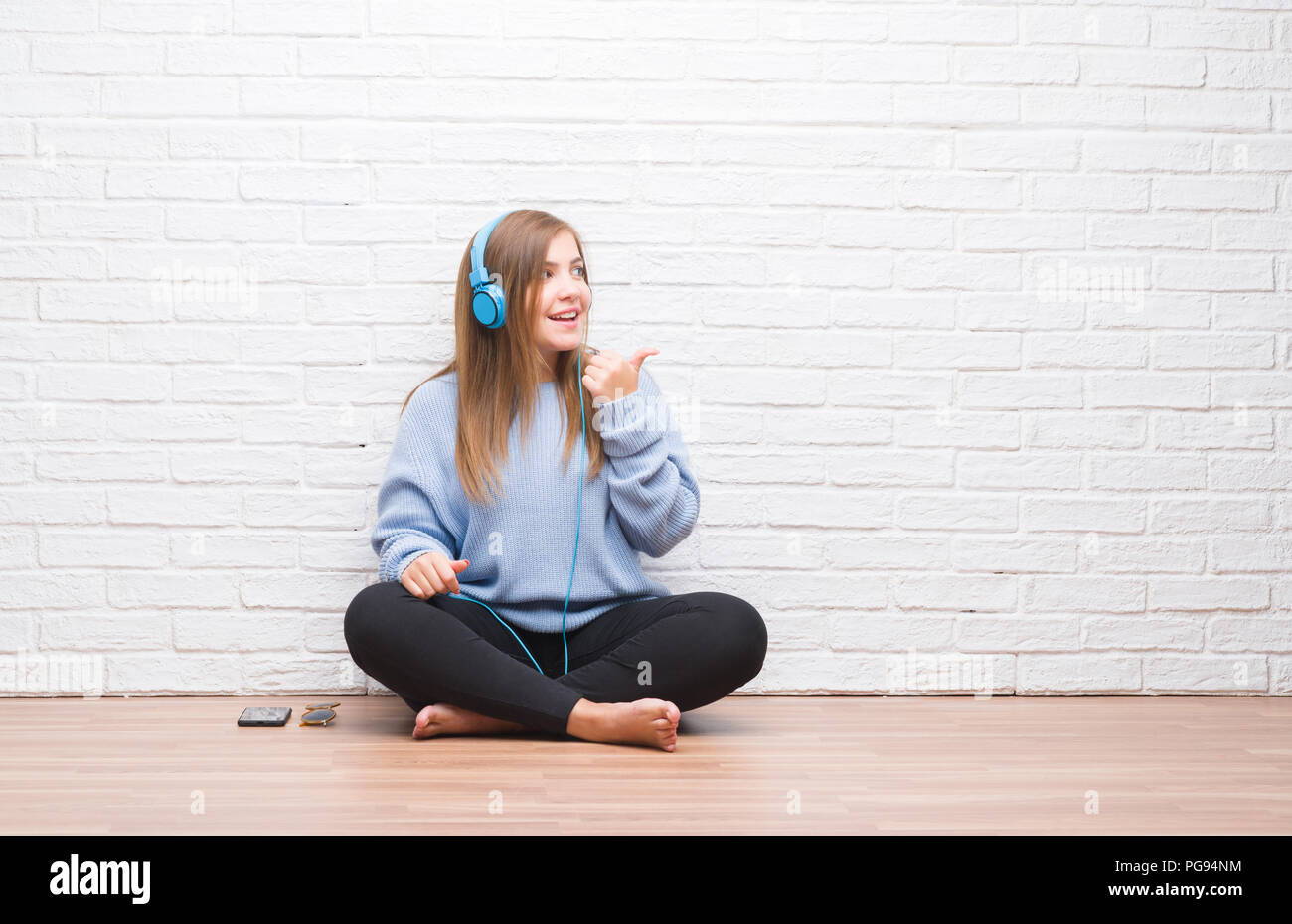 Young adult woman over white brick wall listening music wearing ...