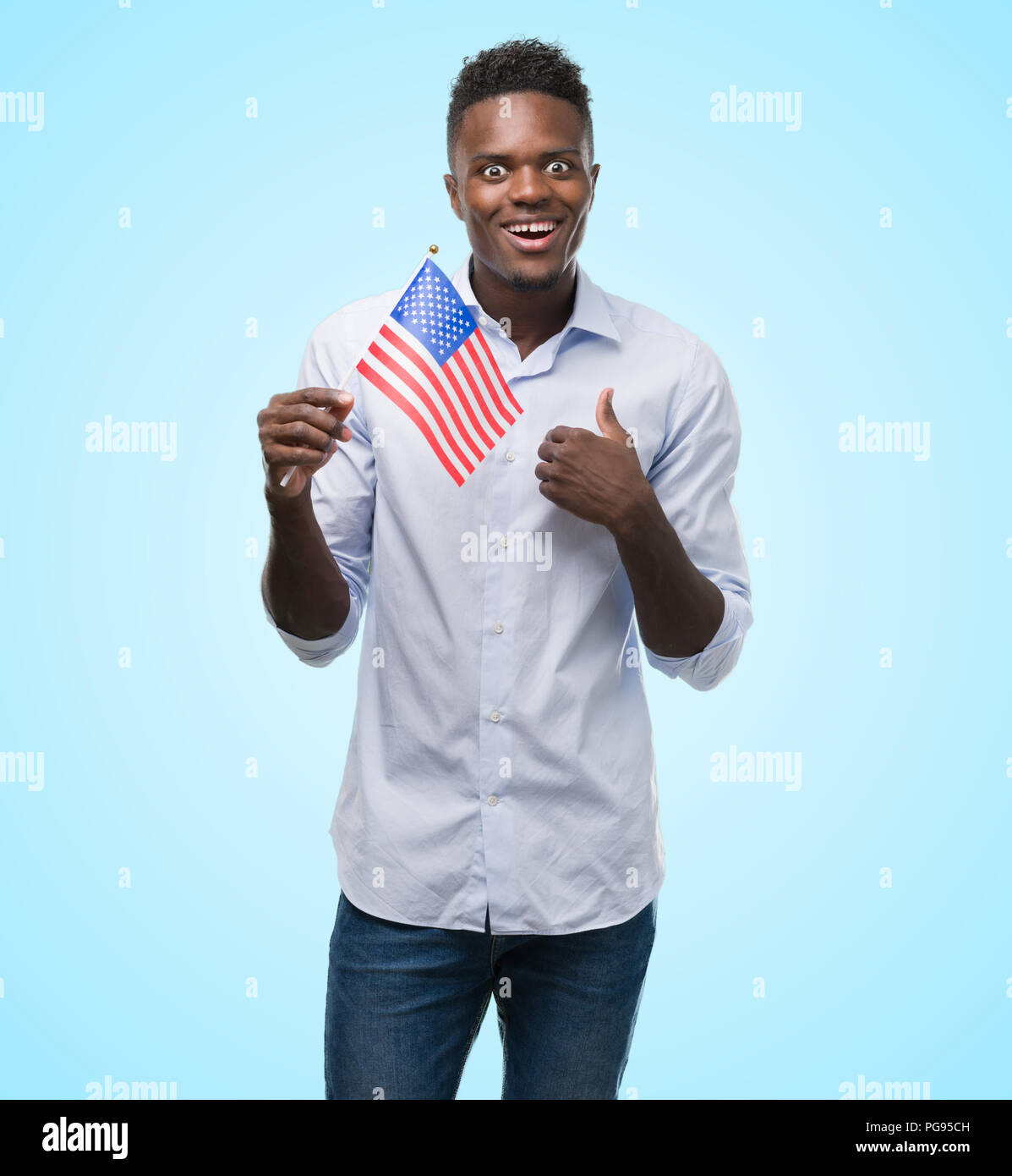 Young african american man holding USA flag with surprise face pointing ...