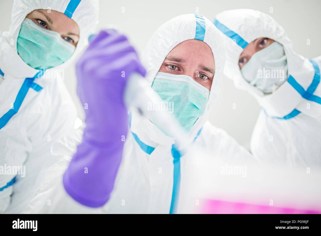 Lab technicians wearing protective suits and face masks in a laboratory that must maintain a sterile environment. Stock Photo