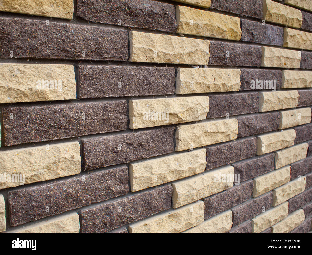 Diagonal view of a wall of yellow and brown bricks close-up as background Stock Photo