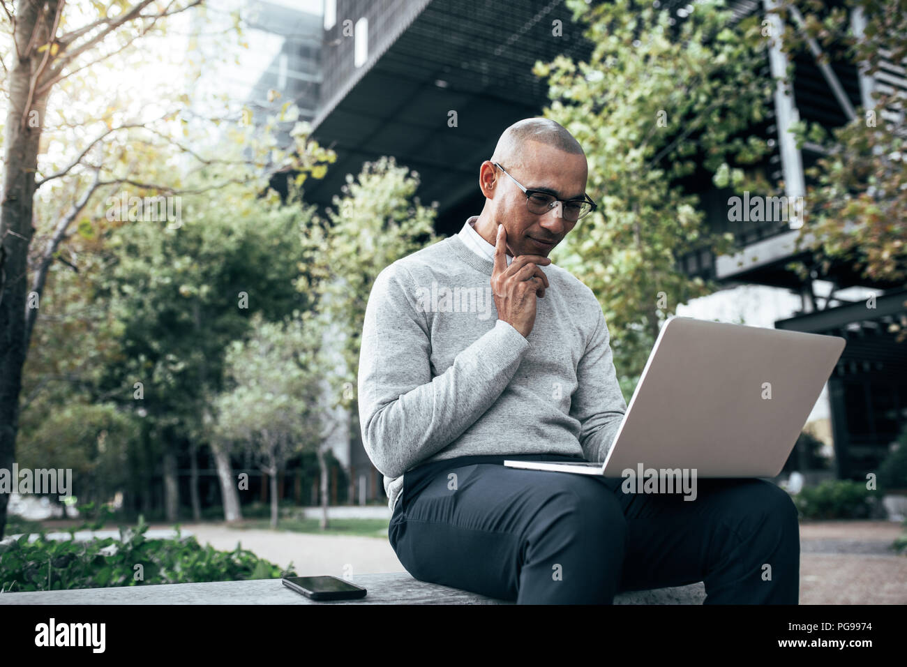 Businessman working on laptop computer sitting outdoors with mobile ...