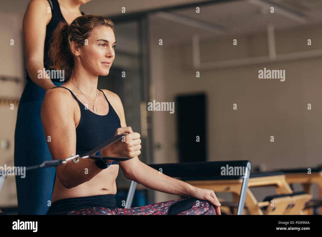 Woman sitting on a pilates training machine pulling stretch band with her hand. Stock Photo