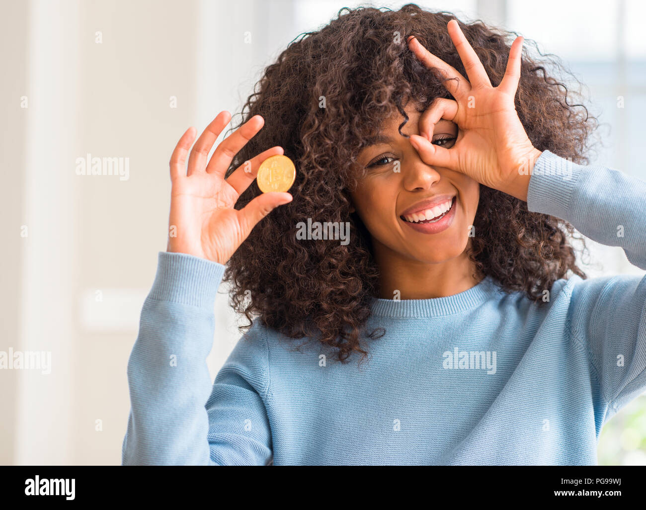 African american woman holding golden bitcoin cryptocurrency at home with  happy face smiling doing ok sign with hand on eye looking through fingers  Stock Photo - Alamy