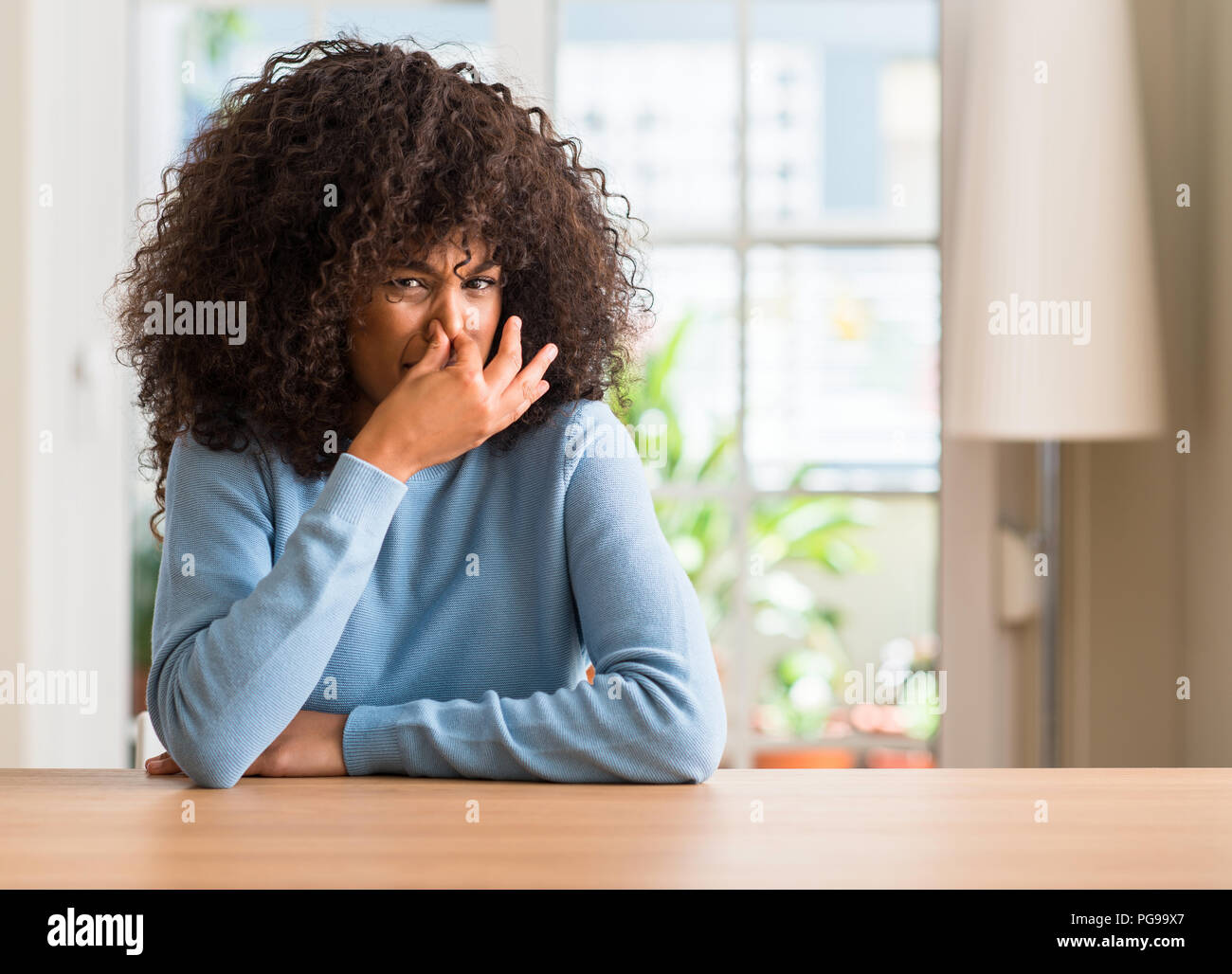 African american woman at home smelling something stinky and disgusting