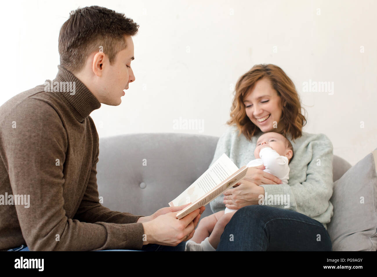 Parents reading book to baby in living room Stock Photo