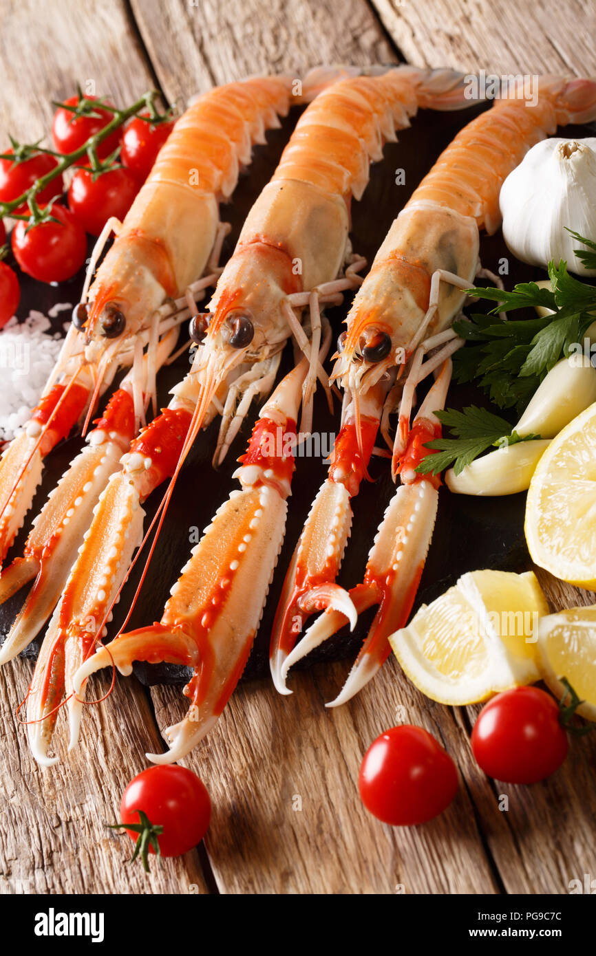 Seafood raw food: scampi or langoustine with vegetables, herbs and spices close-up on the table. Vertical Stock Photo