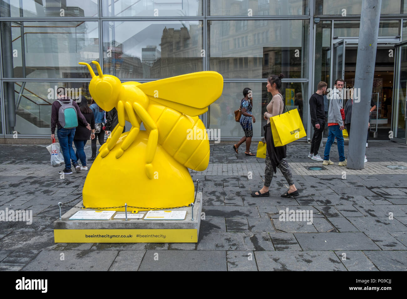 Lady with a large yellow bag walking passed a yellow bee in the city Stock Photo