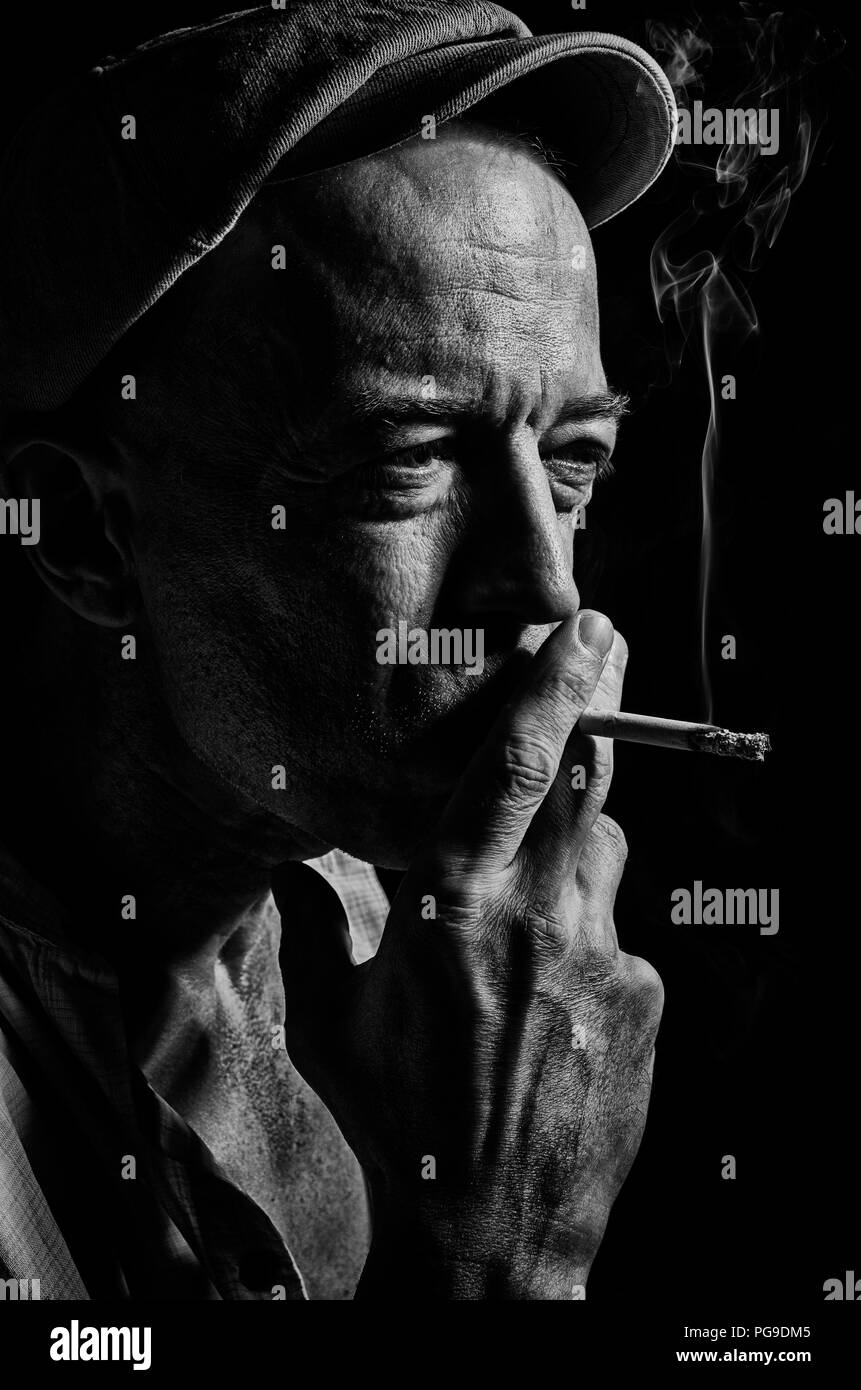 Portrait of elderly man in a cap and with a cigarette on a dark background . Stock Photo