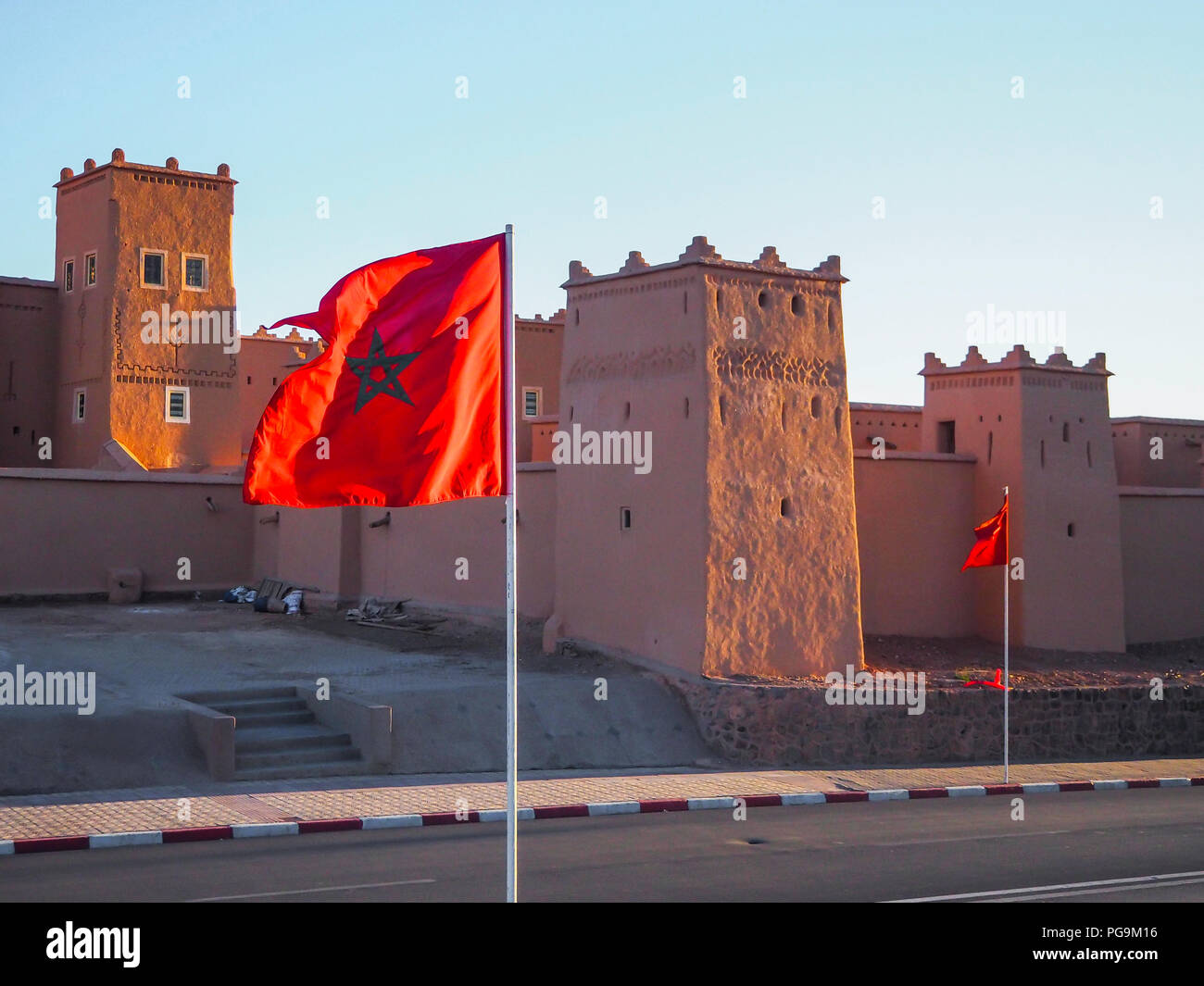 Moroccan flag flying with Ait Benhaddou in the background during sunset Stock Photo