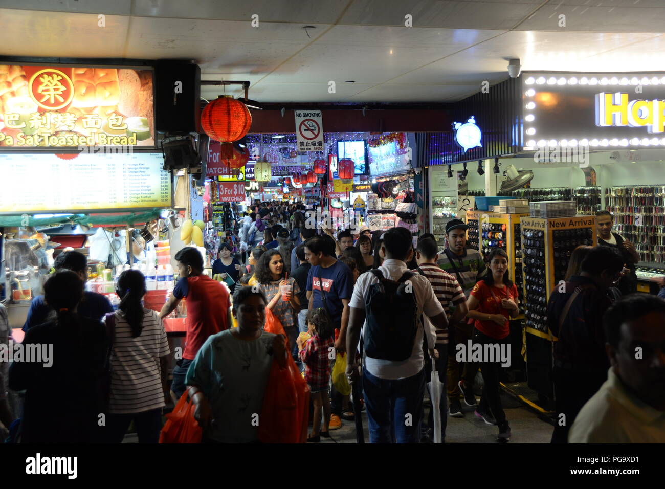 Crowds wander at night near the entrance to this market. Popular with both locals and tourists, Bugis Street Market is well-known for being one of the cheapest places in Singapore to buy souvenirs, accessories, clothes, electronics, houseware and cosmetics. Stock Photo