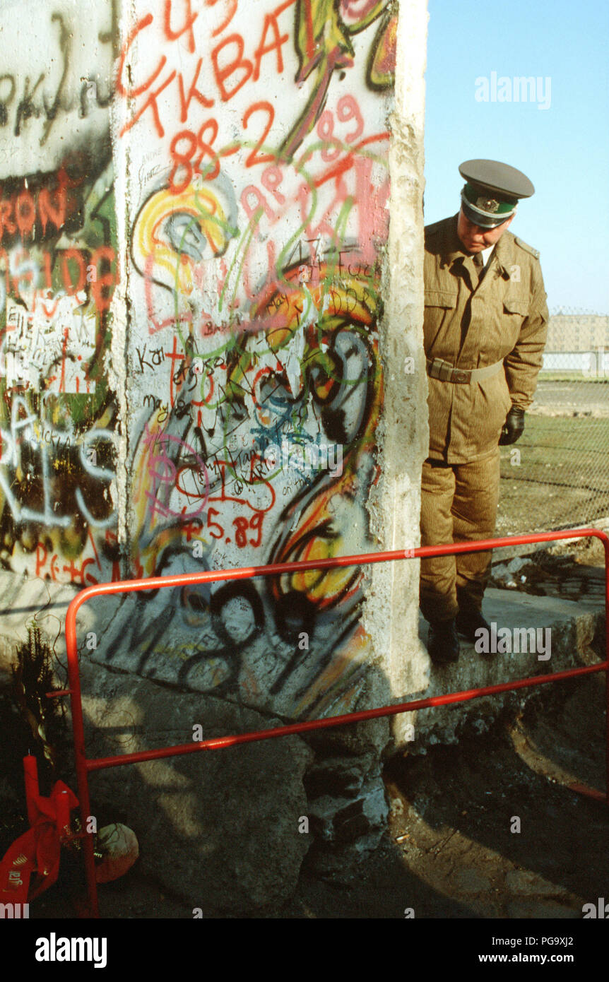 An East German policeman looks at a small Christmas tree adorning the West German side of the Berlin Wall.  The guard is standing at the newly created opening in the Berlin Wall at Potsdamer Platz. Stock Photo