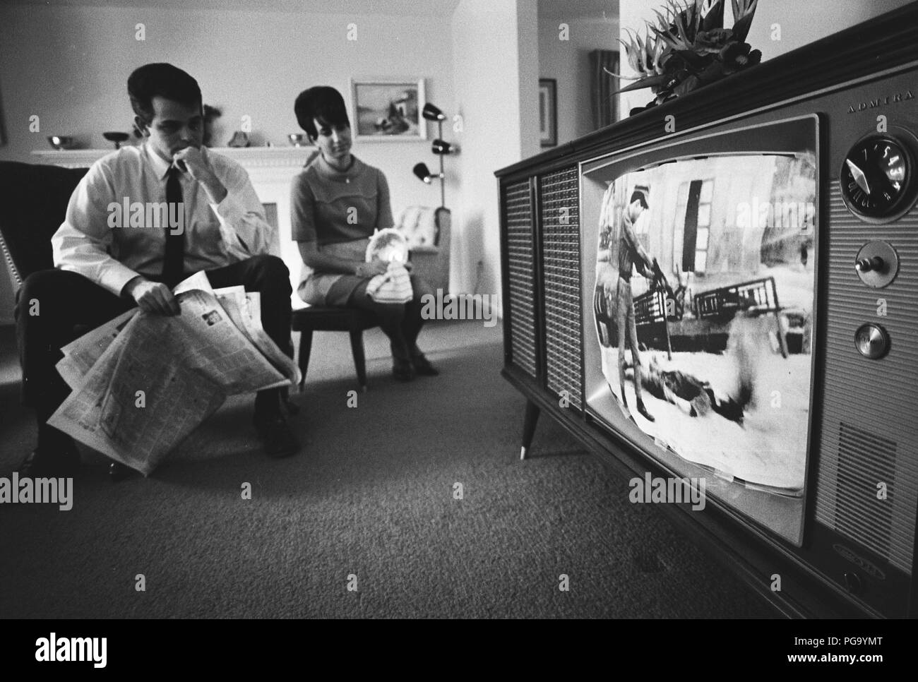 A man and a woman watching tv news film footage of the Vietnam war on a television in their living room Stock Photo