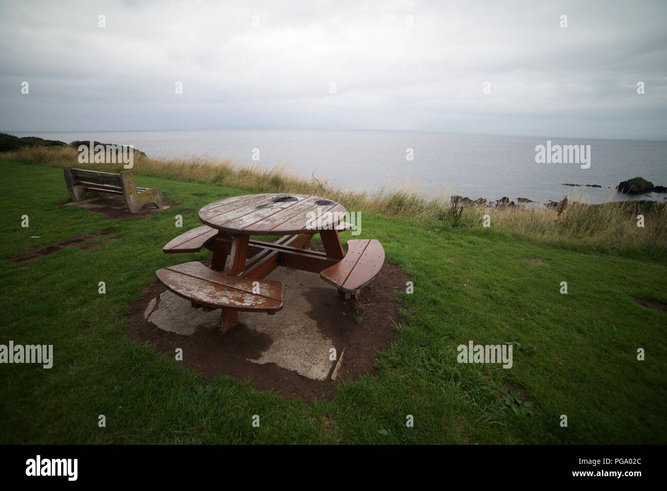 Round Picnic table by the coast with a stunning sea view (Round wooden picnic table and bench) Stock Photo