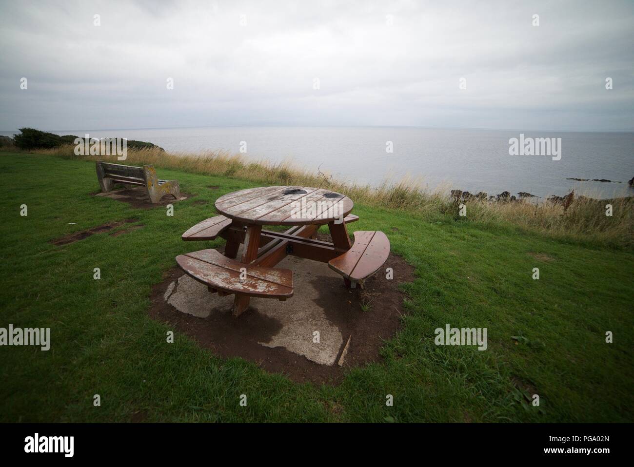 Round Picnic table by the coast with a stunning sea view (Round wooden picnic table and bench) Stock Photo
