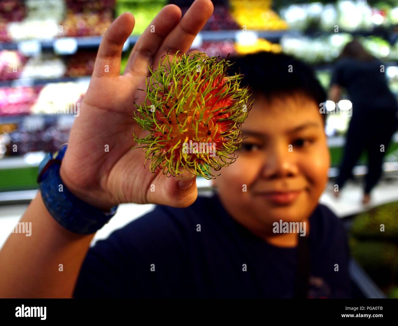 Photo of a young Asian boy holds up a rambutan fruit inside a ...
