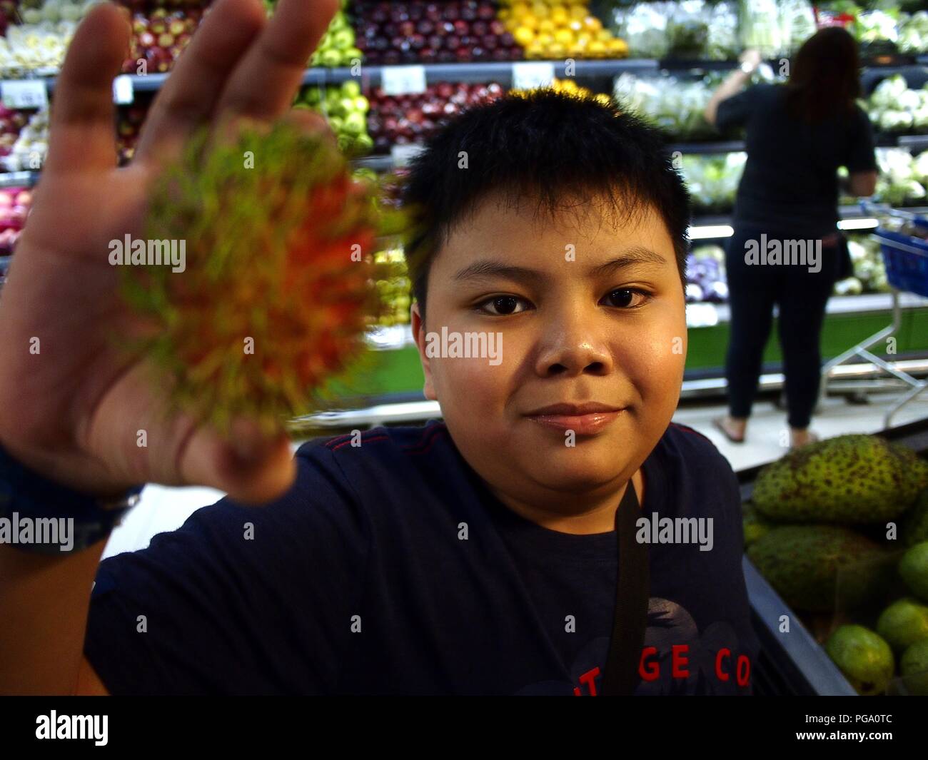 Photo of a young Asian boy holds up a rambutan fruit inside a ...