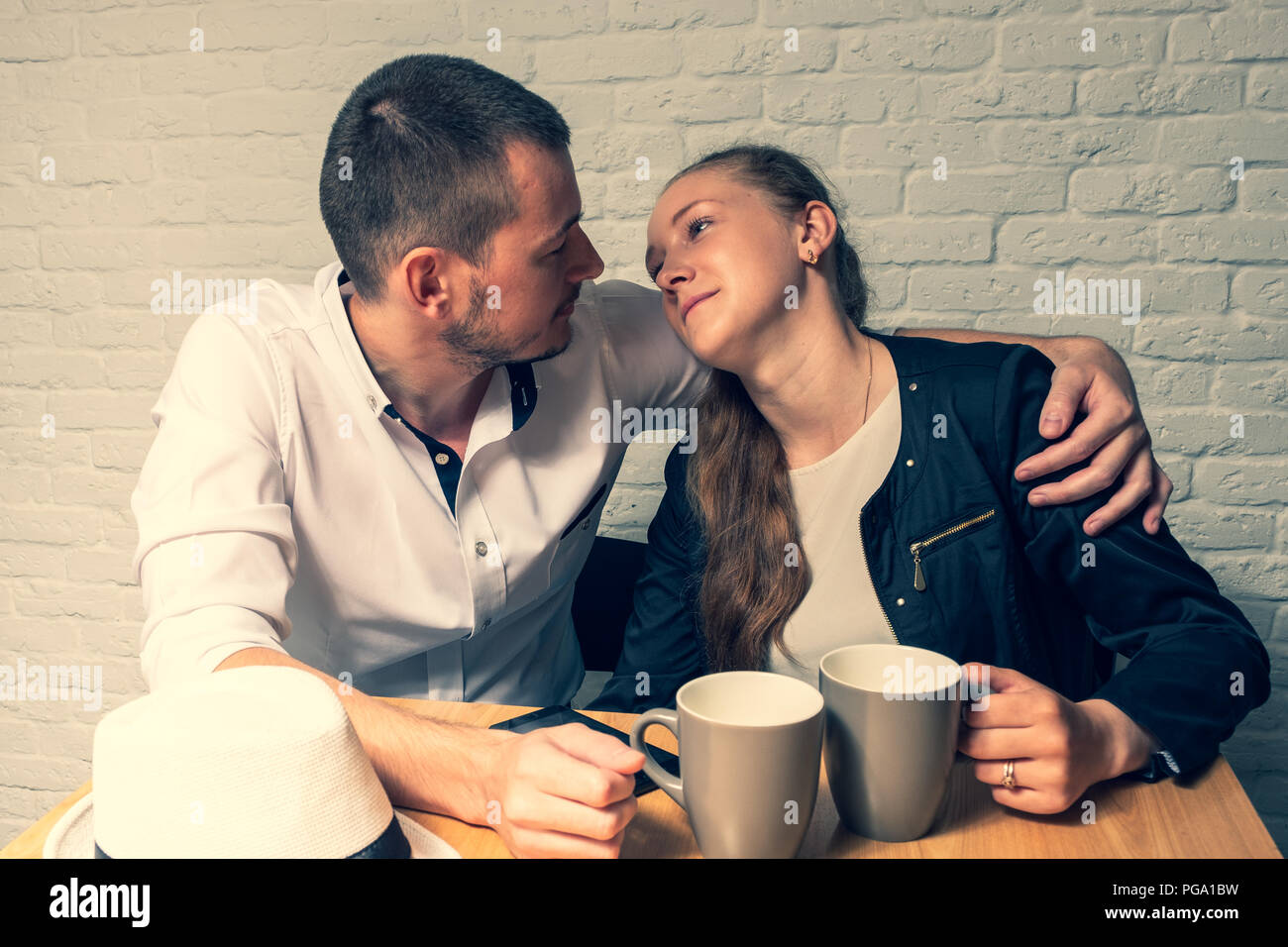 The girl and the guy in cafe, at a table, talk. The guy and the girl with love and tenderness look at each other. The girl put the head on a shoulder  Stock Photo