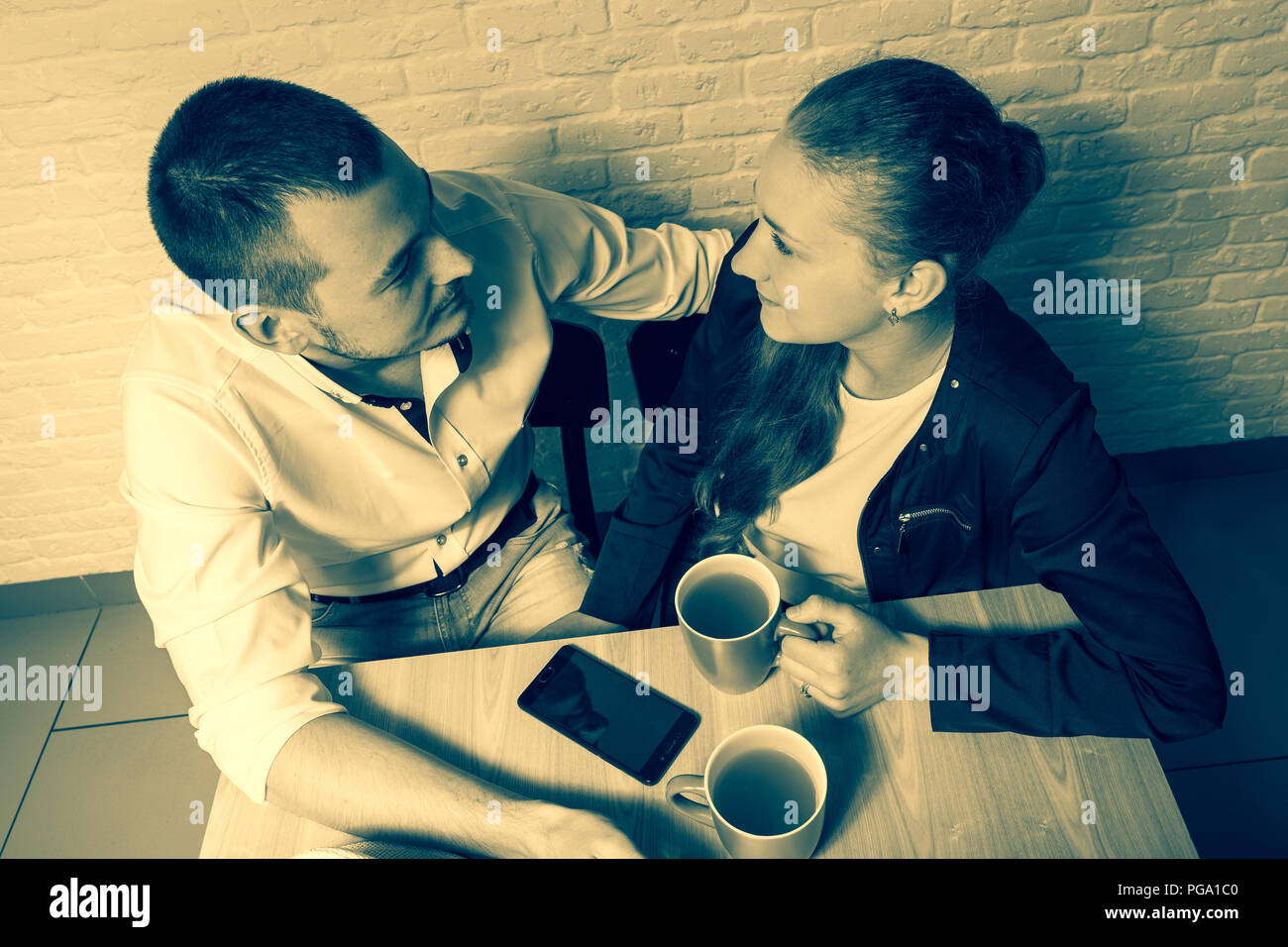 The girl and the guy in cafe, at a table, talk. The guy and the girl with love and tenderness look at each other. On a table there is a tea and phone. Stock Photo