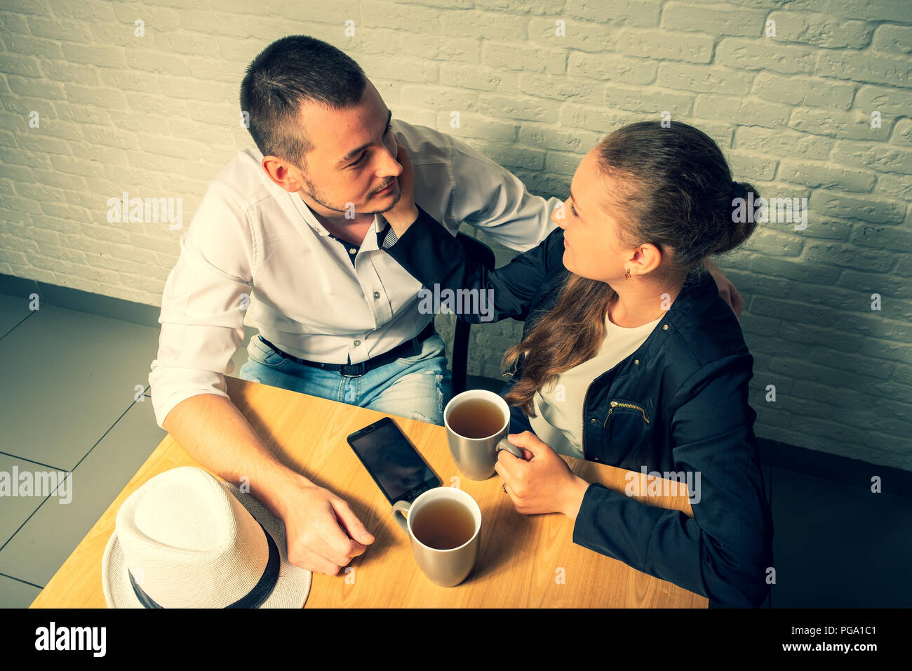 The girl and the guy in cafe, at a table, talk. The guy and the girl with love and tenderness look at each other. On a table there is a tea, phone and Stock Photo