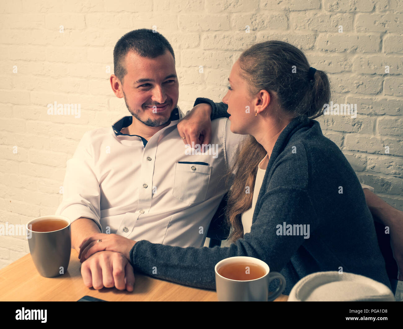 The girl and the guy in cafe, at a table, talk. The guy and the girl with love and tenderness look at each other. Hold hands and look with love at eac Stock Photo