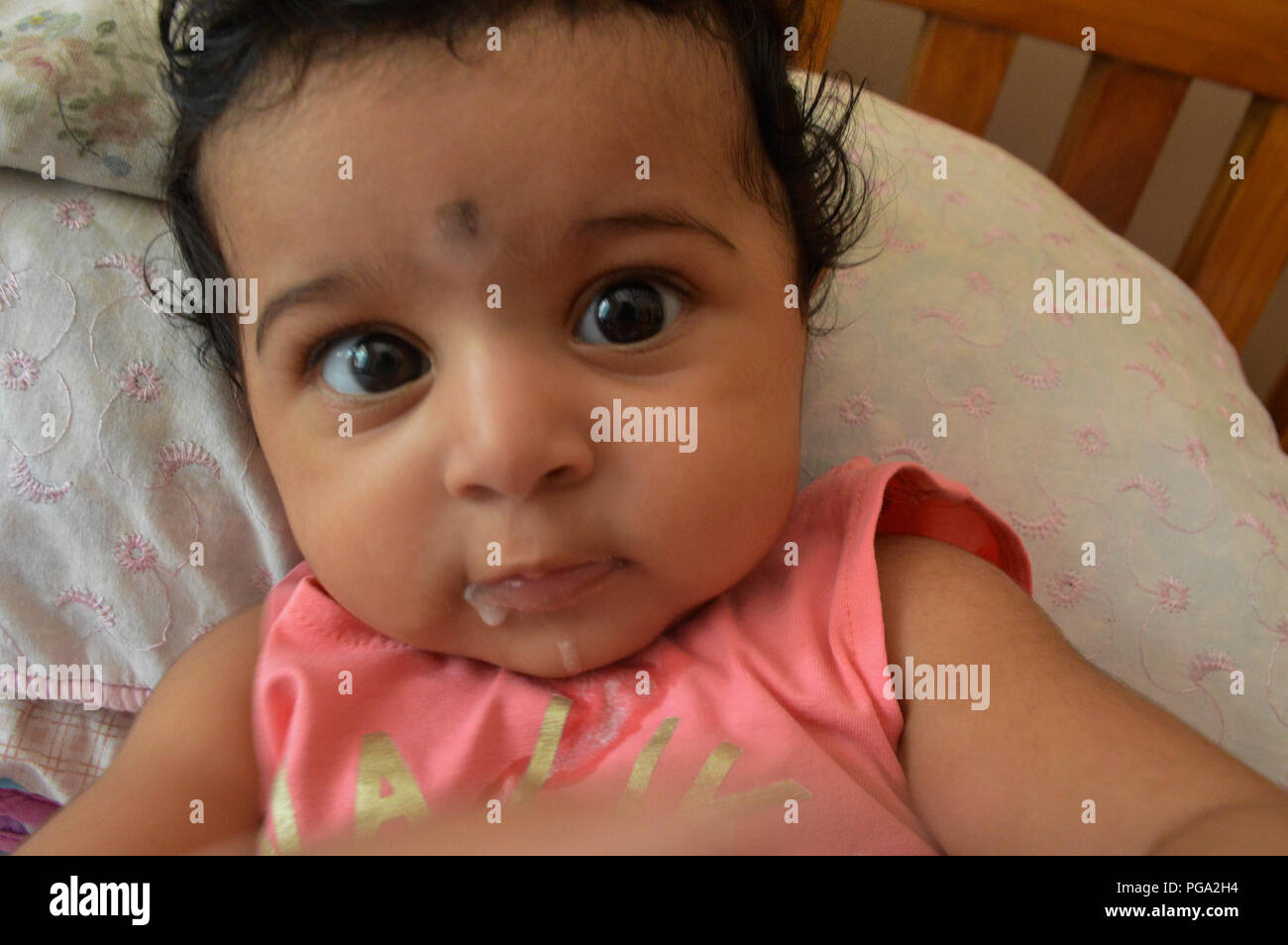 Gig eyed infant in pink lying on bed looking into the camera in wonder Stock Photo