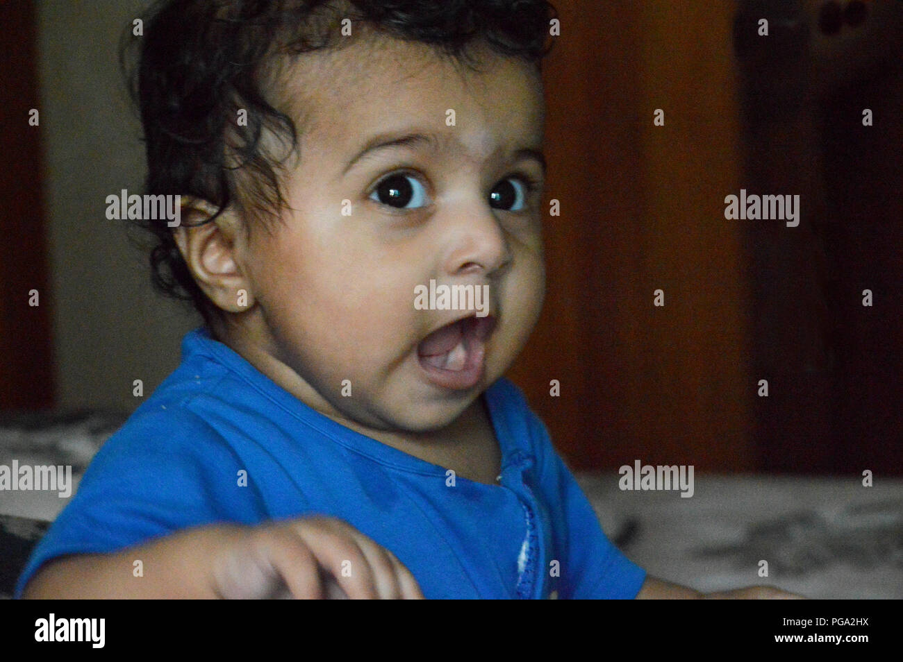 Big eyed infant in Blue shirt singing with her mouth wide open Stock Photo