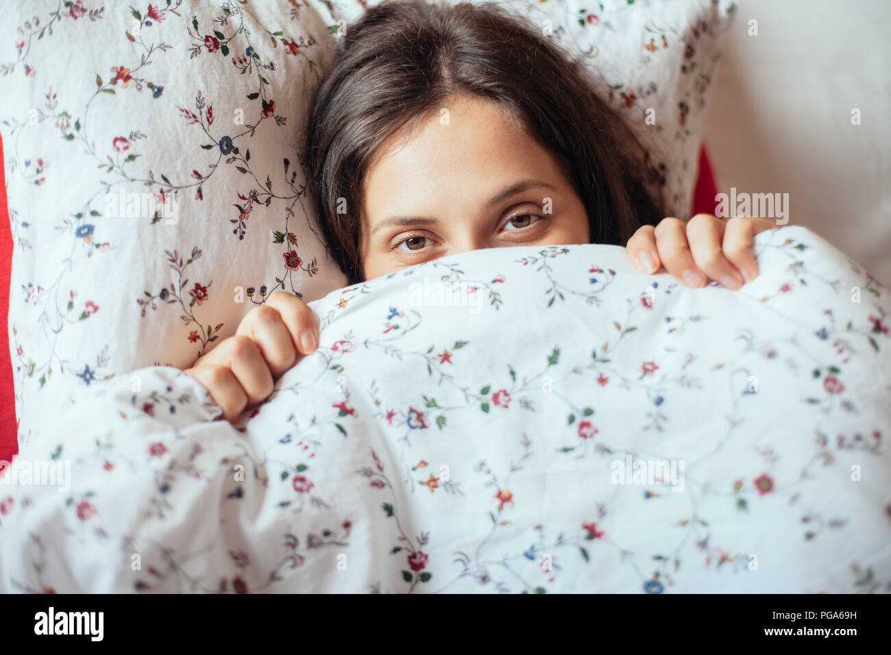 Young girl look under blanket in her bed, closeup. Beautiful woman hiding face Stock Photo