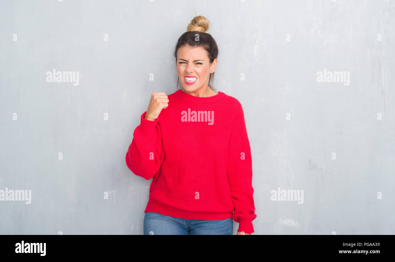 Young adult woman over grey grunge wall wearing winter outfit angry and ...