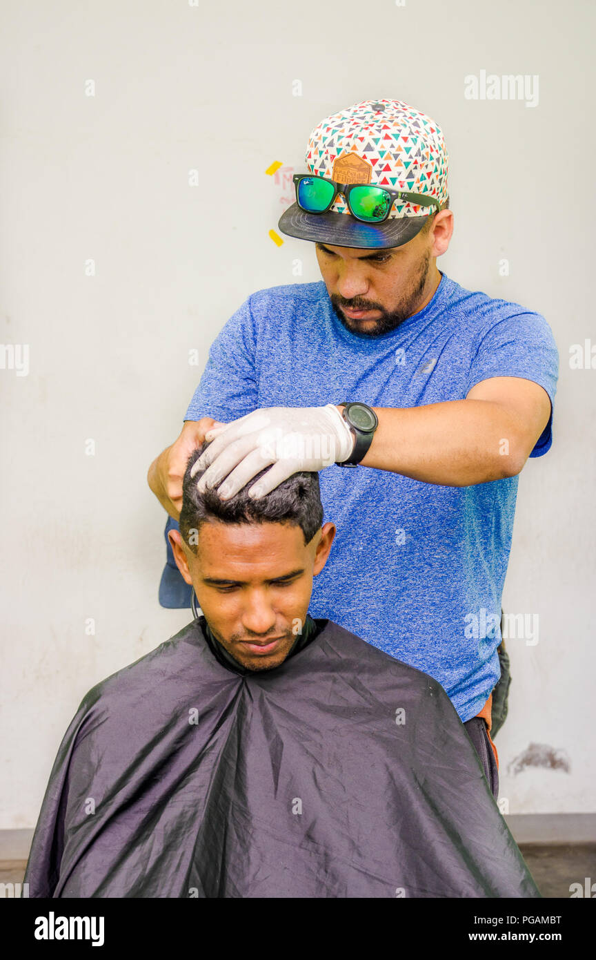 QUITO, ECUADOR, AUGUST 21, 2018: Outdoor view of unidentified man wearing gloves and hat, using a cut hair machine in a youg guy, inside of a refuge f Stock Photo