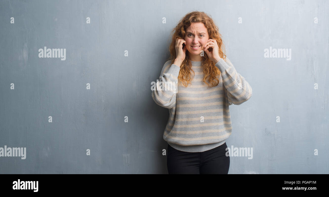 Young Redhead Woman Over Grey Grunge Wall Covering Ears With Fingers With Annoyed Expression For 